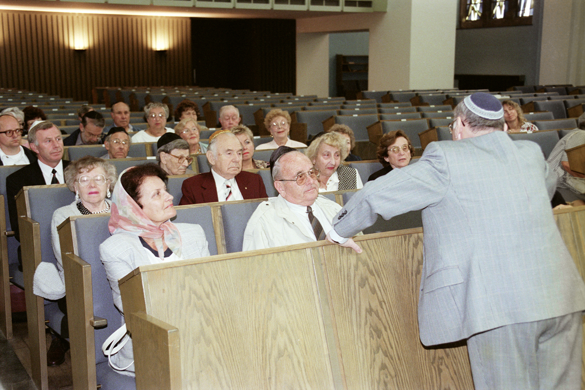 Besucher sitzen in der Synagoge, ein Mann steht vor ihnen und redet