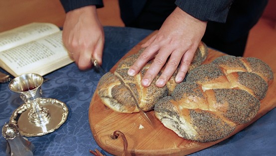 Zwei Hände schneiden Brot, auf dem Tisch steht ein Kelch