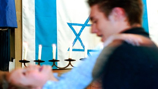 Zwei Personen tanzen, im Hintergrund sieht man die Fahne von Israel