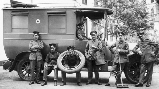 Acht Sanitäter in altmodischen Uniformen vor einem historischen Krankenwagen